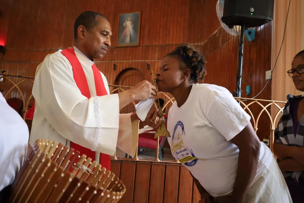 Une femme incline la tête pour embrasser une croix offerte par un reverend à l’église Saint Clair dans la région de Ti Plas Kazo, Port-au-Prince, le vendredi 18 avril 2025. Photo par Dieugo André pour The Haitian Times.