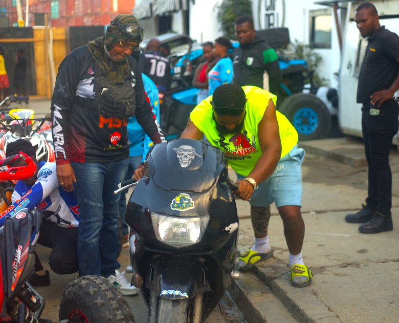 Un homme pousse une moto le long du trottoir avant le début de la Ruff Ryders Block Party le 7 mars 2026, à Cap-Haïtien. Photo par Onz Chéry / The Haitian Times.
