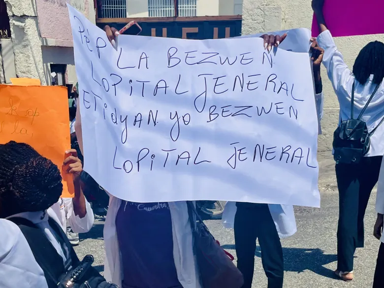 Student protesters hold placards bearing messages saying that people and students need the State University Hospital and demanding its relocation from a gang-controlled area in Port-au-Prince on Wednesday, July 1, 2026. Photo by Jhakenson Blaise/The Haitian Times.