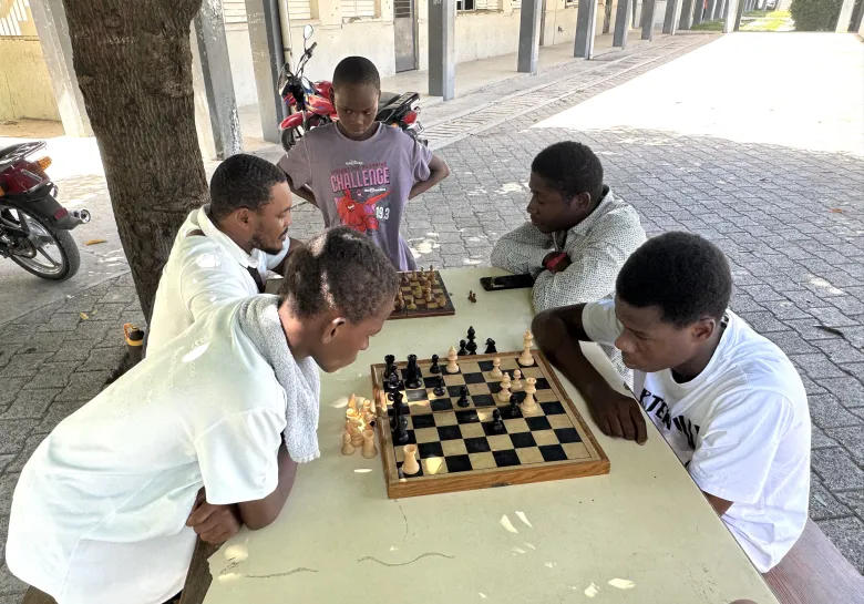Two young men and children play chess during “Let’s Play Together” on Saturday, Aug. 15, 2026, at Lycée Anacaona in Léogâne, Haiti. Photo by Daniella Saint-Louis for The Haitian Times. 
