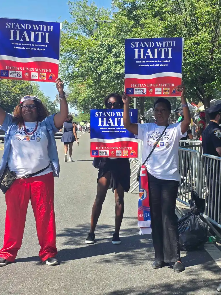 Yolette Williams de l’Alliance haïtienne-américaine, au centre, défile avec deux femmes portant une pancarte réclamant la restauration du TPS pour les Haïtiens lors de la parade du Jour des Antilles à Brooklyn, le 7 septembre. Photo de Darlie Gervais pour The Haitian Times.